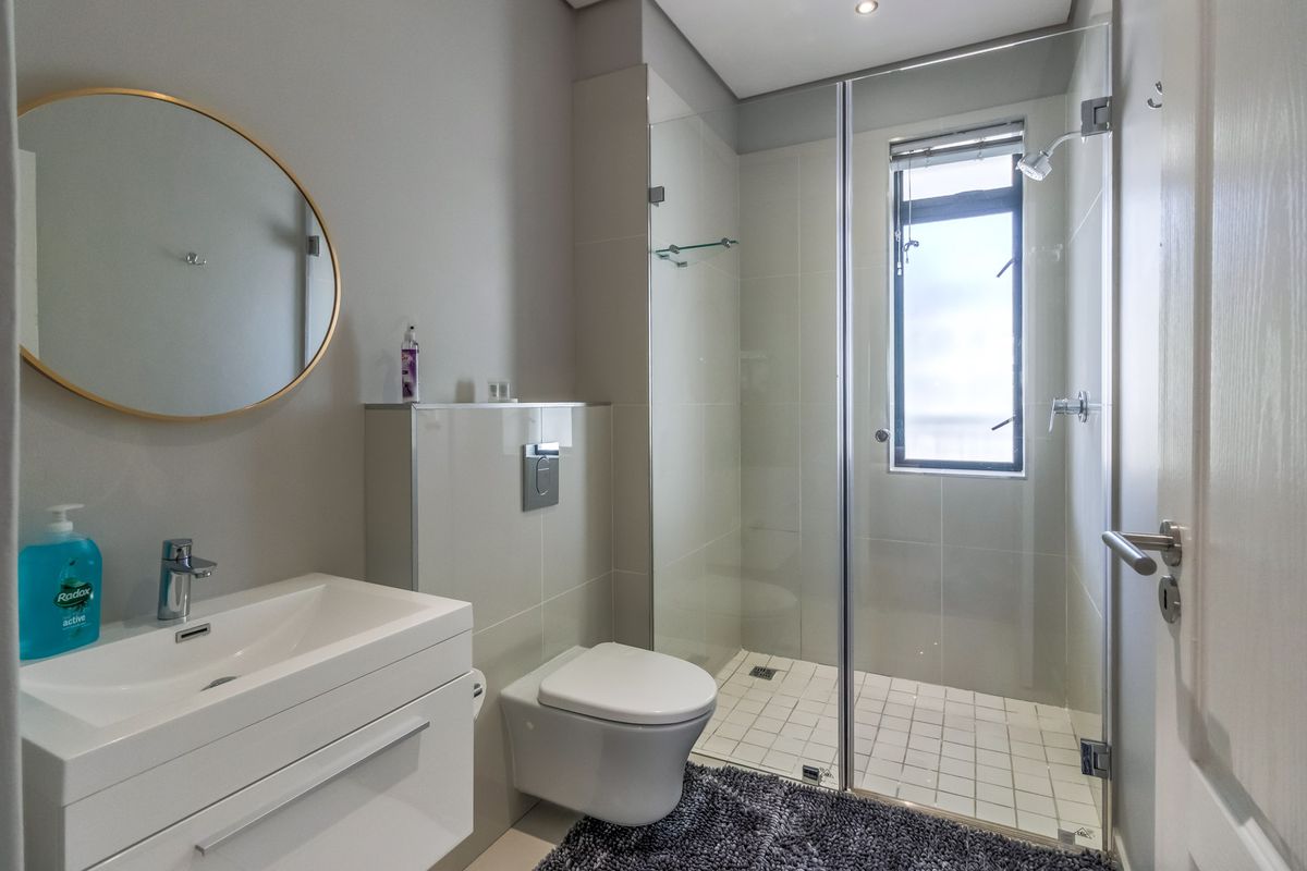 Modern bathroom featuring a wall-mounted vanity, wall-hung toilet with concealed cistern, and a glass-enclosed shower with tiled flooring.