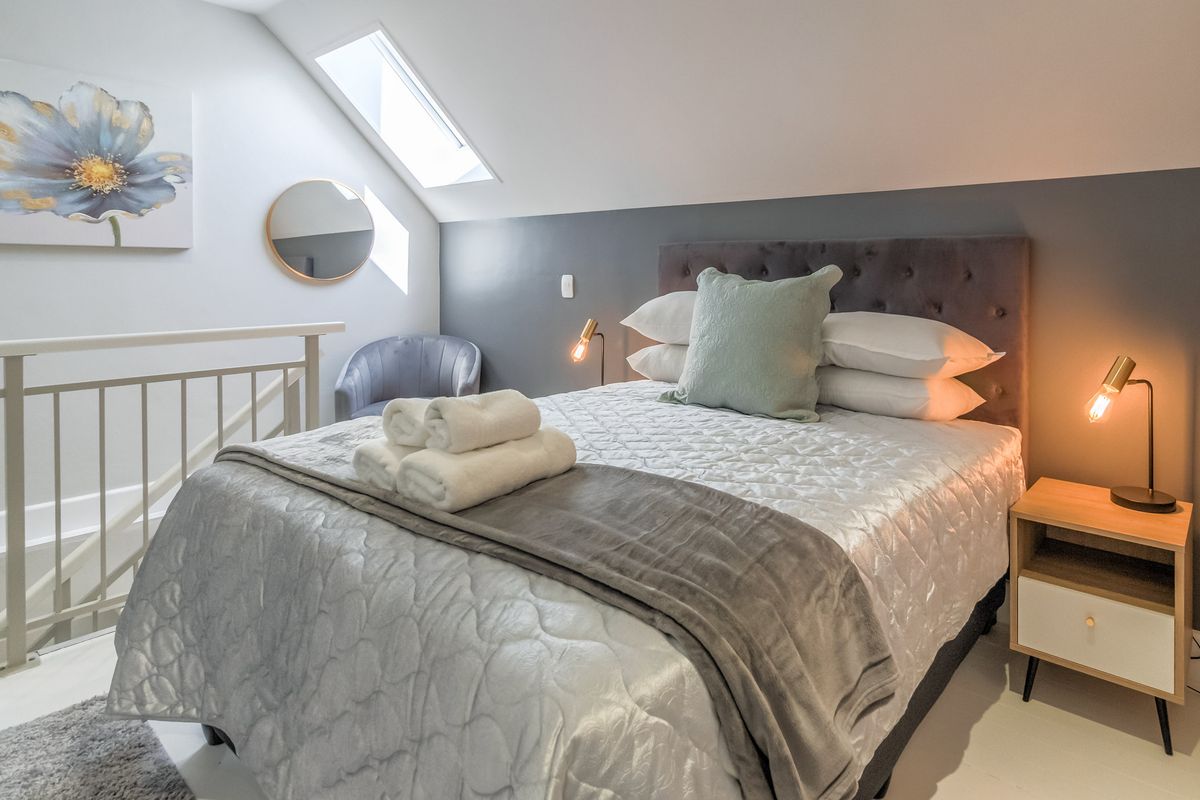A well-lit bedroom featuring a sloped ceiling, a skylight, and a protective railing overlooking the lower level.