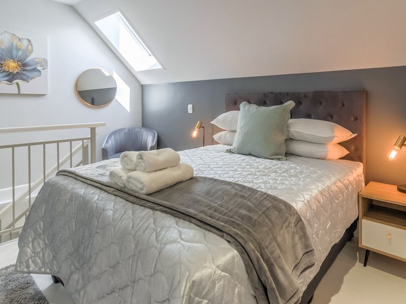 A well-lit bedroom featuring a sloped ceiling, a skylight, and a protective railing overlooking the lower level.