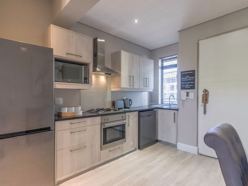 Modern kitchen featuring light wood cabinetry, dark countertops, integrated appliances including a gas hob, oven, and microwave, with neutral finishes throughout.