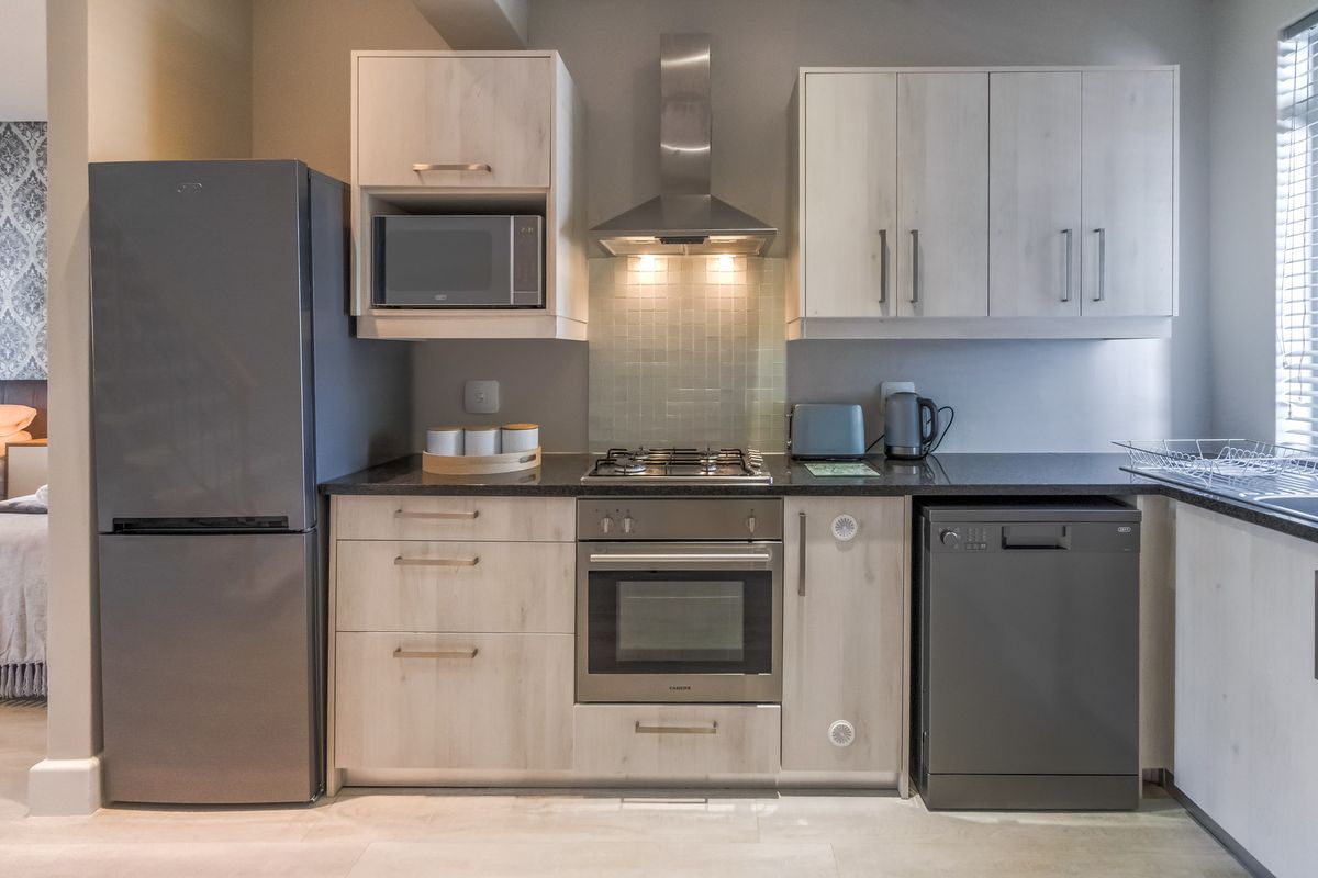 Modern kitchen featuring light wood cabinetry, granite countertops, a gas hob, built-in oven, stainless steel extractor fan, and integrated dishwasher.