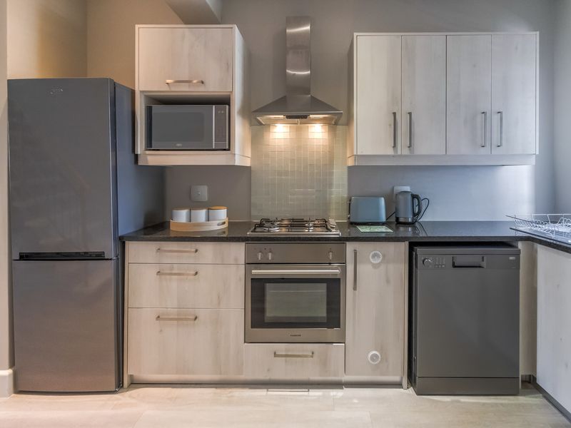 Modern kitchen featuring light wood cabinetry, granite countertops, a gas hob, built-in oven, stainless steel extractor fan, and integrated dishwasher.