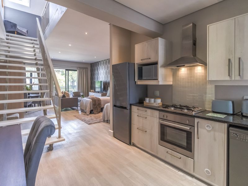 Modern open-plan apartment featuring a sleek kitchen with built-in appliances, light wood cabinetry, and a staircase leading to an upper level.