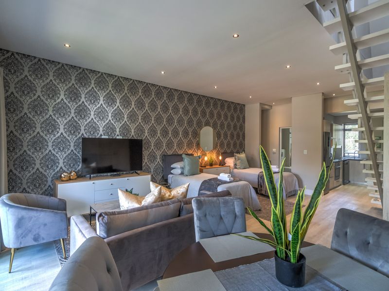 A spacious open-plan apartment featuring a combined living, dining, and bedroom area with modern finishes, laminate flooring, and an open-tread staircase.