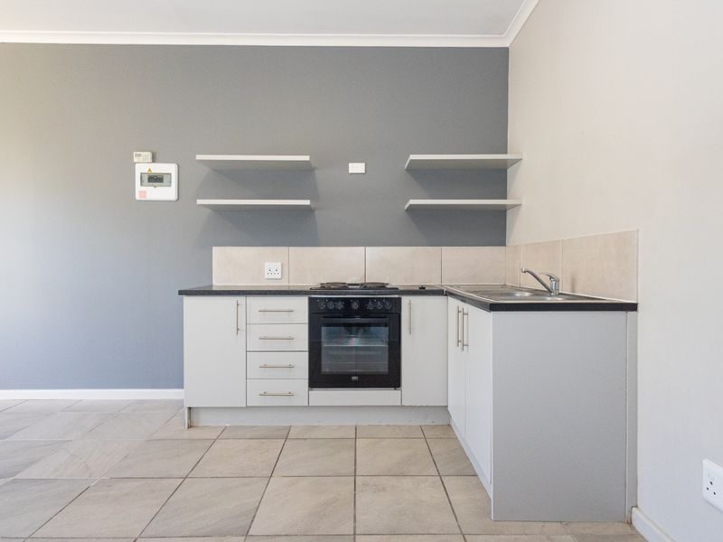 A compact, modern kitchen featuring built-in oven, electric hob, tiled backsplash, and neutral cabinetry, presented in a clean, empty space.