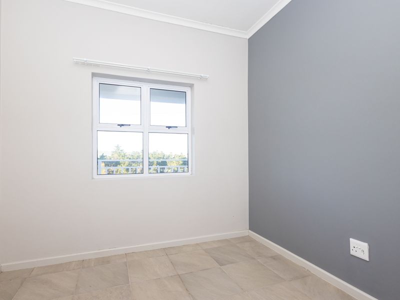 A clean, empty bedroom featuring neutral wall tones, a grey accent wall, tiled flooring, and a window with a fitted curtain rod.