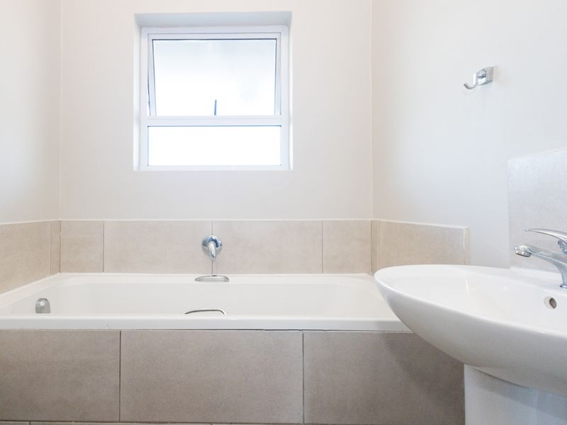 A clean, modern bathroom featuring a built-in bathtub with tiled surround, a pedestal basin with chrome mixer tap, and a top-hung window.