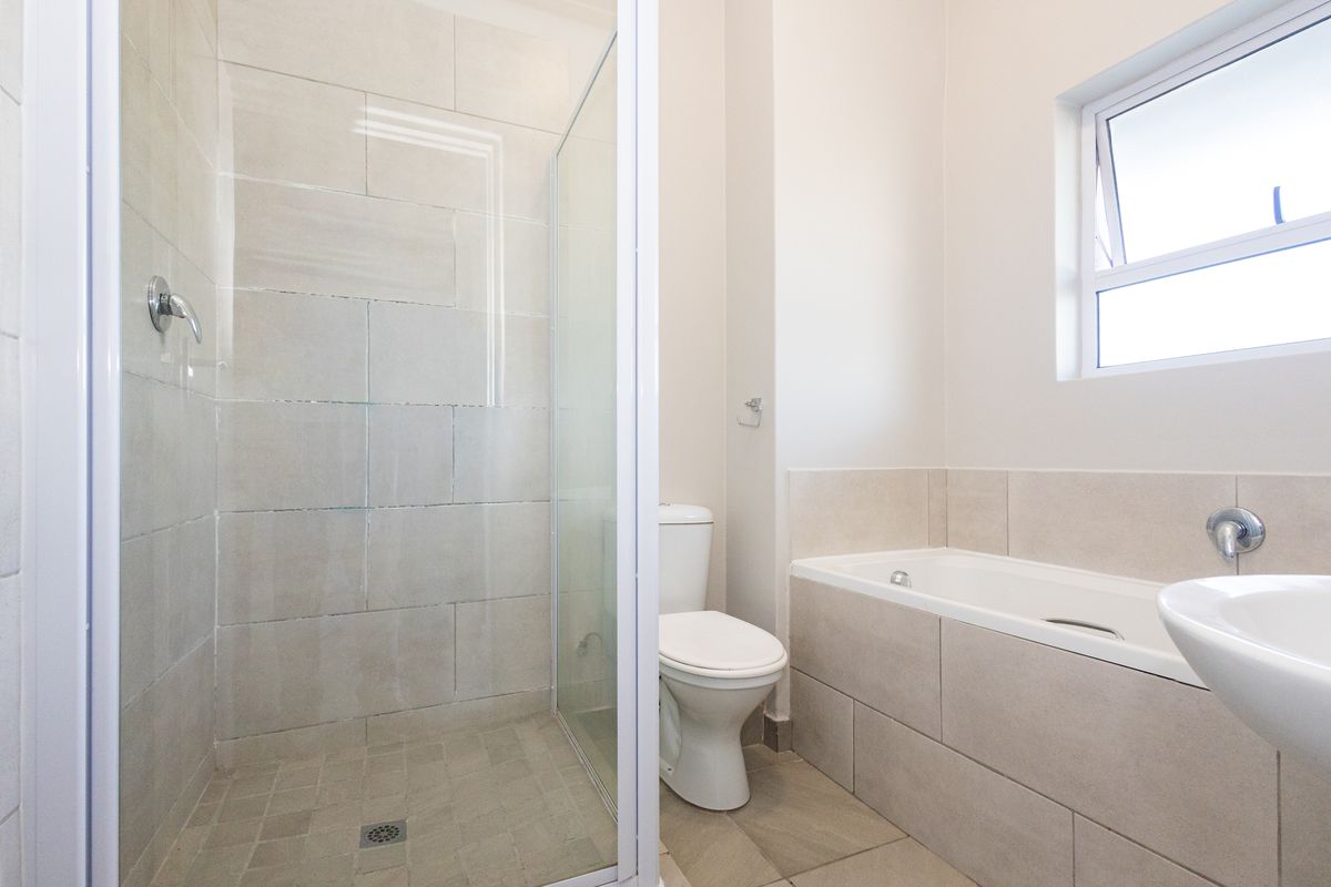 A clean, modern bathroom featuring a separate glass-enclosed shower, a built-in bathtub, and neutral ceramic tiling throughout.