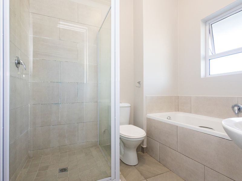 A clean, modern bathroom featuring a separate glass-enclosed shower, a built-in bathtub, and neutral ceramic tiling throughout.