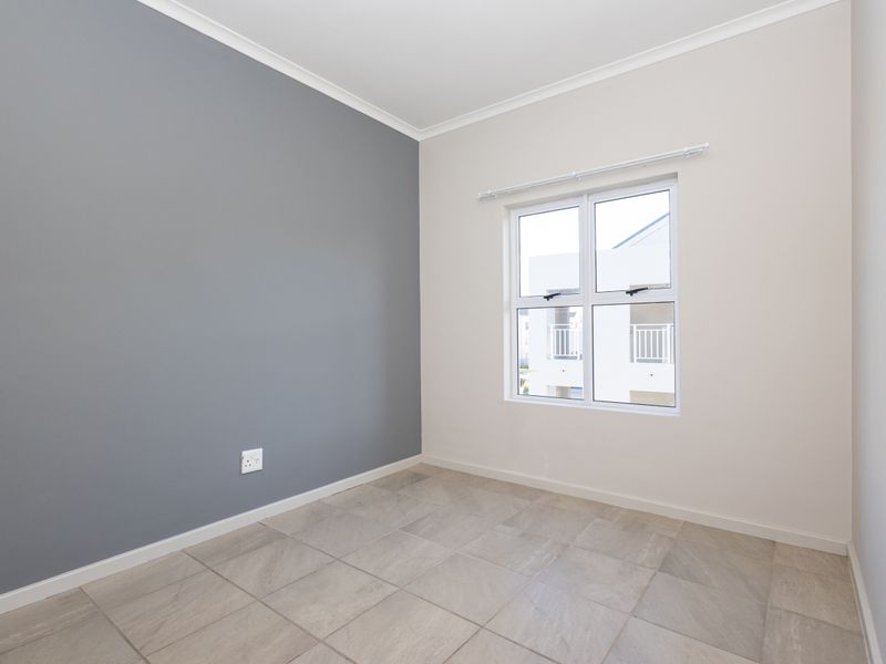 A clean, empty bedroom featuring neutral-toned walls, tiled flooring, and a window with a curtain rod, ready for personalization.