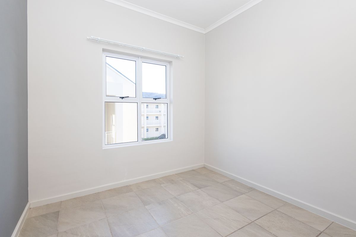 A bright, empty bedroom featuring neutral tiled flooring, clean white walls, and a modern aluminium window frame.