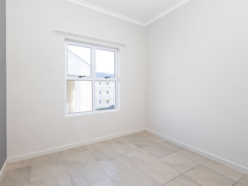 A bright, empty bedroom featuring neutral tiled flooring, clean white walls, and a modern aluminium window frame.