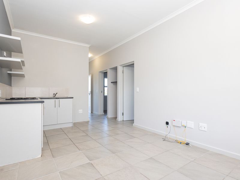 An open-plan living and kitchen area featuring tiled flooring, built-in cabinetry with a hob, and floating shelves, offering a clean, neutral space.