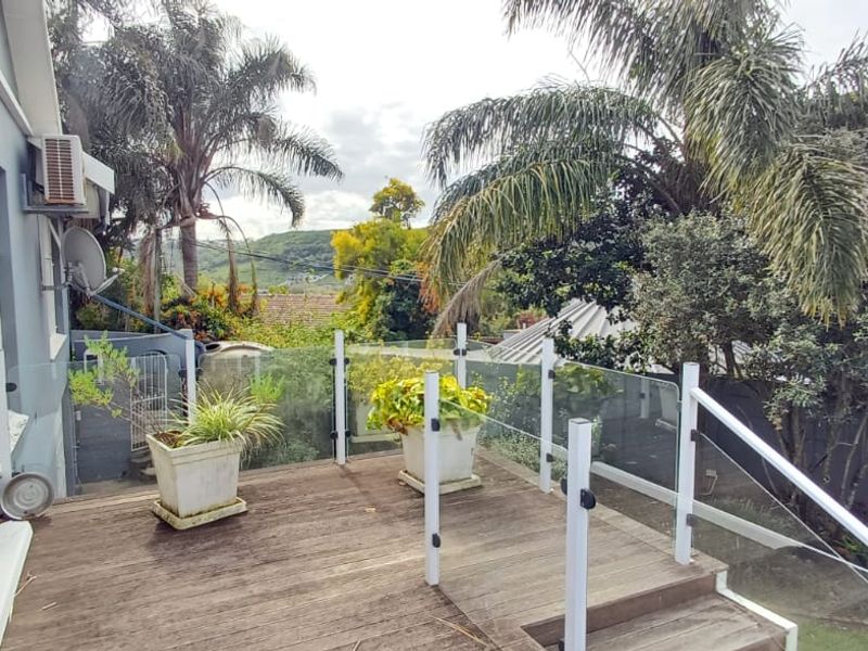 An elevated timber deck featuring a modern glass balustrade, providing an outdoor space with views of the surrounding garden and landscape.