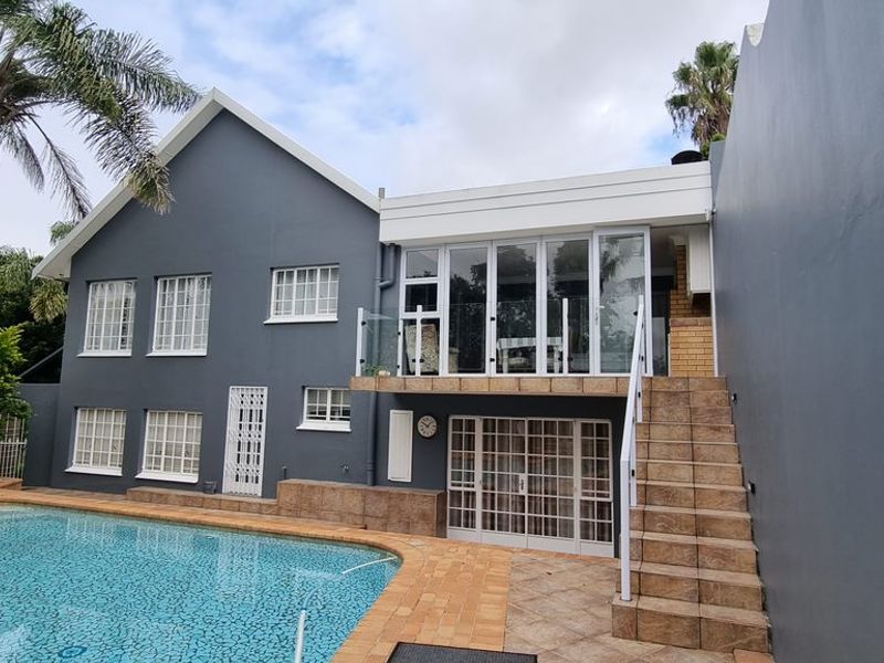 Rear exterior view featuring a swimming pool, paved patio area, external staircase with glass balustrade, and access to the main dwelling.
