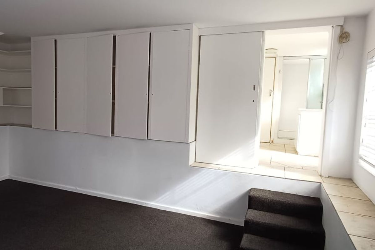 An empty bedroom featuring built-in cabinetry, integrated shelving, and a raised platform area with carpet flooring and venetian blinds.