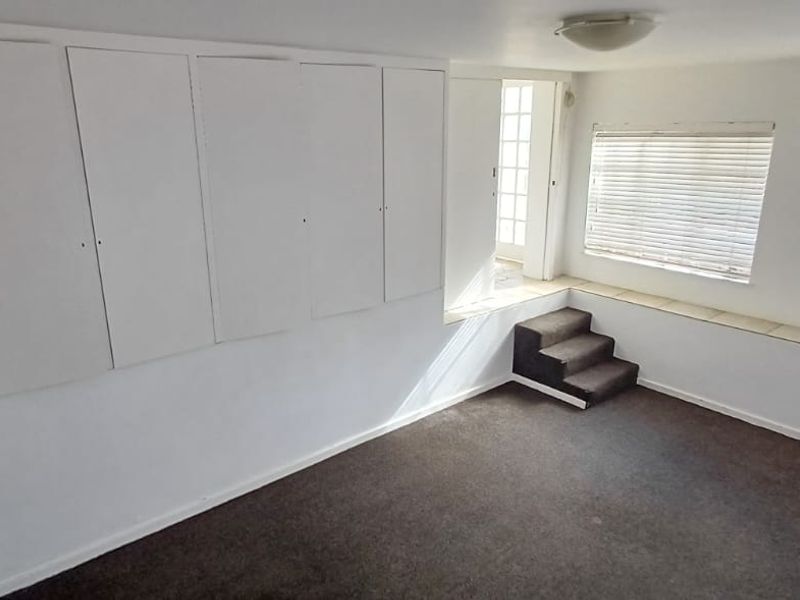 An empty living room featuring built-in cabinetry, shelving, a raised platform area, and large windows with venetian blinds.