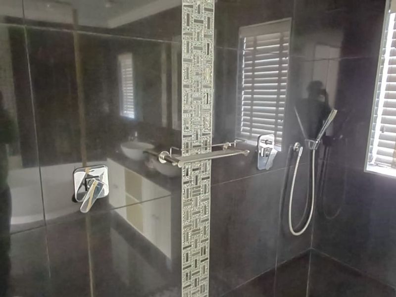 Modern bathroom featuring a walk-in shower with dark wall tiles, a decorative mosaic feature strip, chrome fixtures, and venetian blinds.