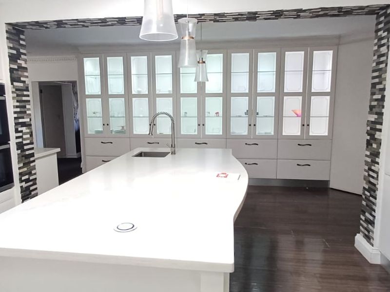 Modern kitchen featuring a large central island, built-in double oven, extensive glass-front cabinetry with integrated lighting, and dark hardwood flooring.