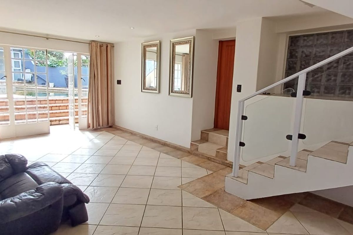 Spacious living area featuring tiled floors, a modern staircase with glass balustrade, and direct access to the outdoor pool area through french doors.