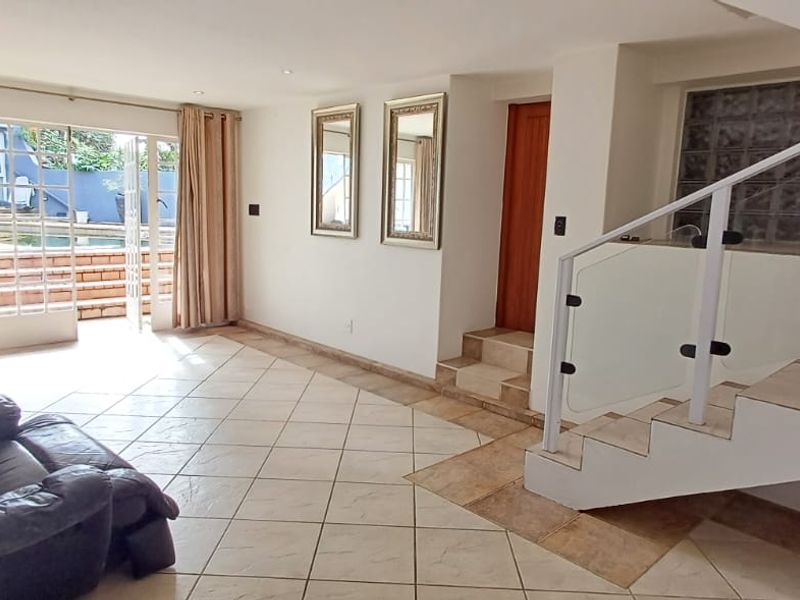 Spacious living area featuring tiled floors, a modern staircase with glass balustrade, and direct access to the outdoor pool area through french doors.