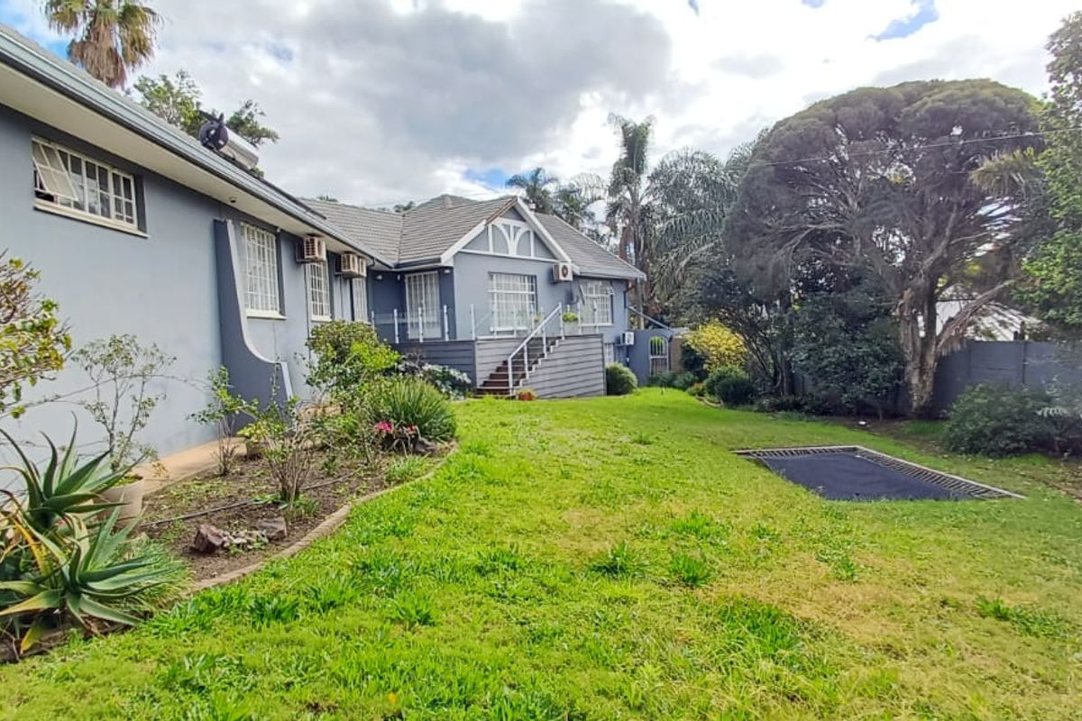 Rear view of the property featuring a landscaped garden, raised timber deck with glass balustrade, and exterior building finishes.
