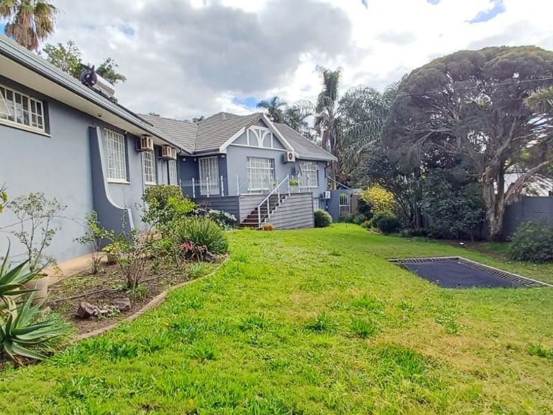 Rear view of the property featuring a landscaped garden, raised timber deck with glass balustrade, and exterior building finishes.