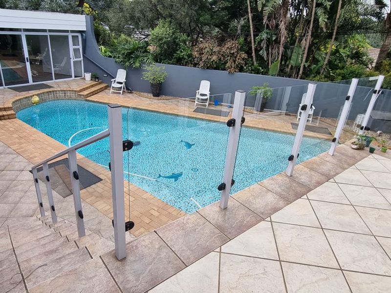 Outdoor pool area featuring a paved patio, glass balustrade safety fencing, and direct access to the main dwelling through sliding glass doors.