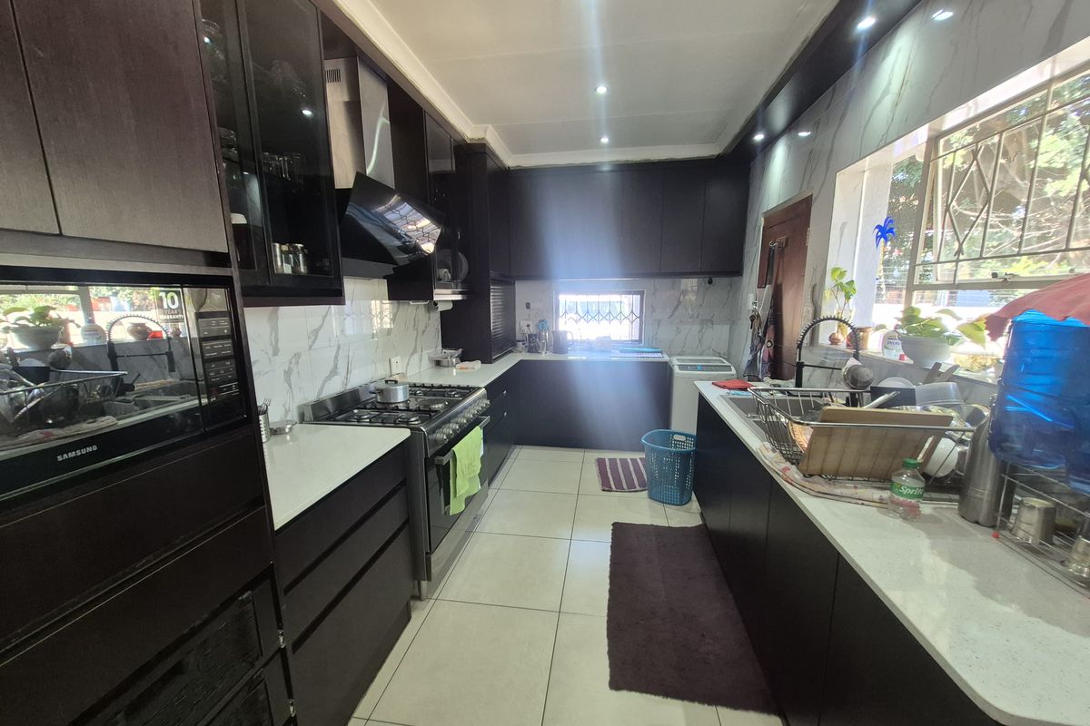 Modern kitchen featuring dark cabinetry, stone countertops, marble-look splashbacks, and a gas stove with an integrated extractor fan.