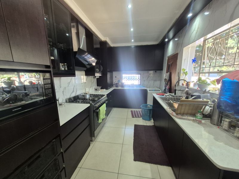 Modern kitchen featuring dark cabinetry, stone countertops, marble-look splashbacks, and a gas stove with an integrated extractor fan.