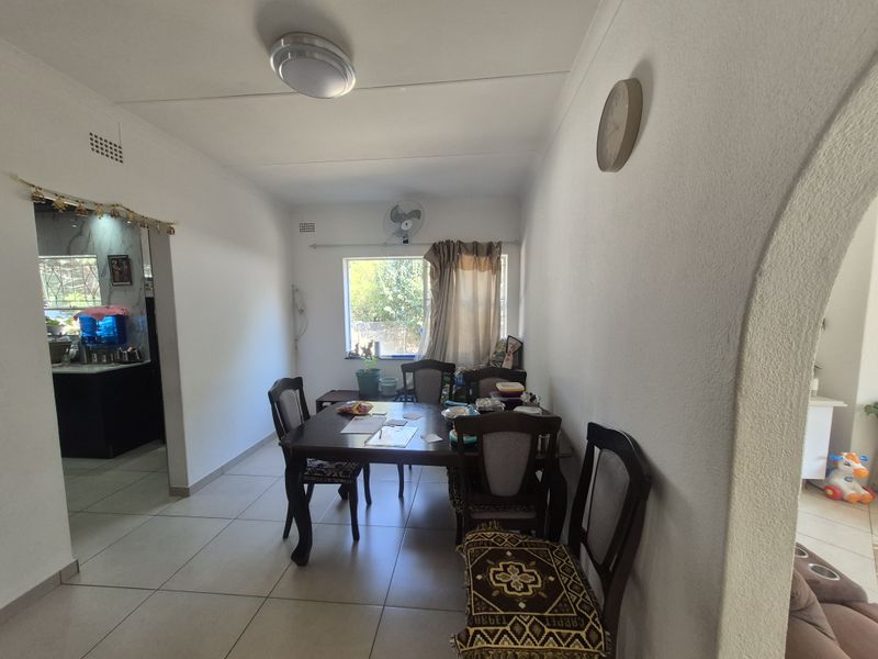 A dining room featuring tiled flooring, a decorative archway, and a wall-mounted ventilation fan, providing a functional space adjacent to the kitchen area.