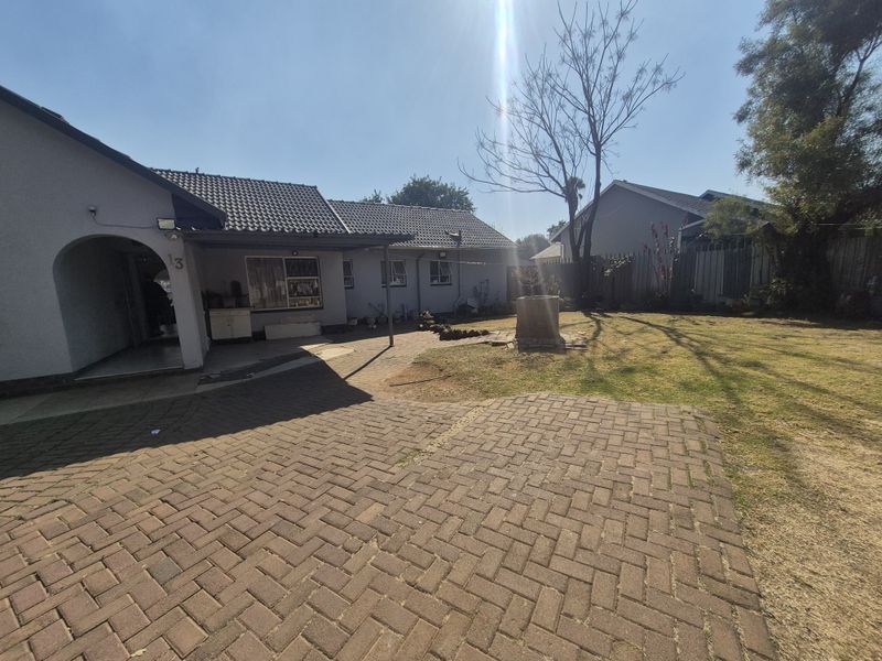 Rear view of the property featuring a paved courtyard, covered patio area, and a spacious garden with established lawn.