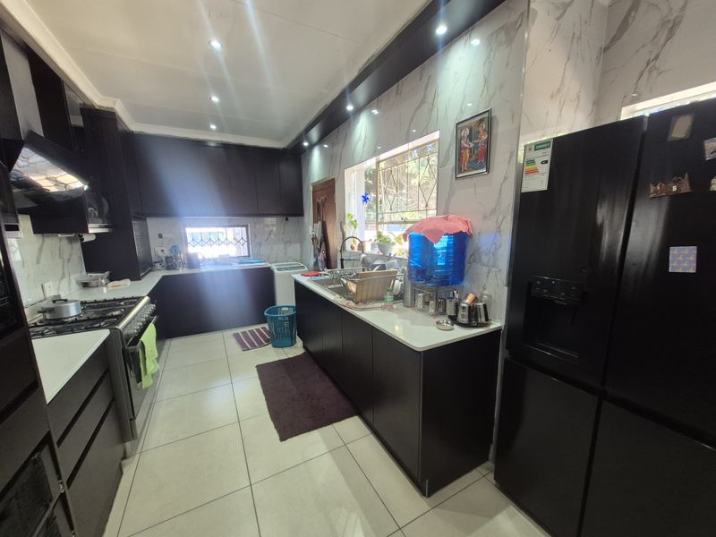 Modern kitchen featuring dark cabinetry, stone countertops, marble-look wall tiles, and a gas stove with an integrated extractor fan.