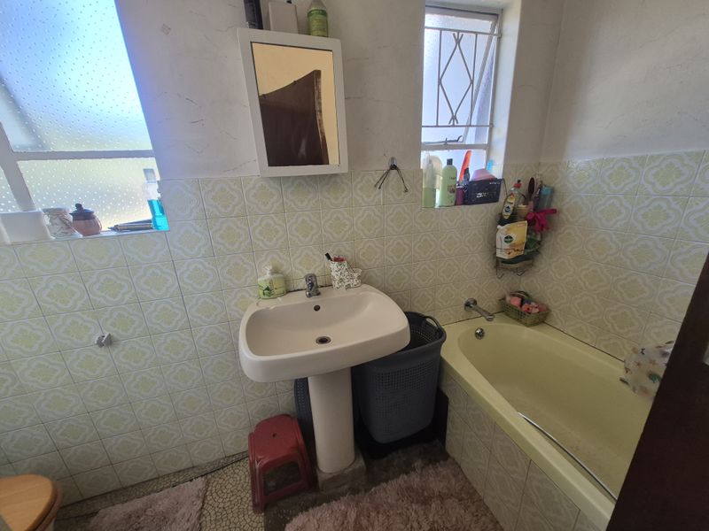 A dated bathroom featuring a pedestal washbasin, built-in bathtub, and patterned wall tiles, requiring modernization to improve aesthetic appeal and functionality.