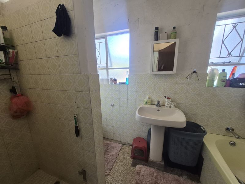 A dated bathroom featuring a pedestal washbasin, bathtub, and original tiled finishes, offering significant potential for a modern renovation.