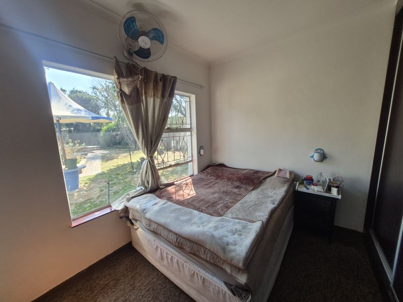 A bedroom featuring a large window with security bars, a wall-mounted fan, and built-in wardrobe storage.