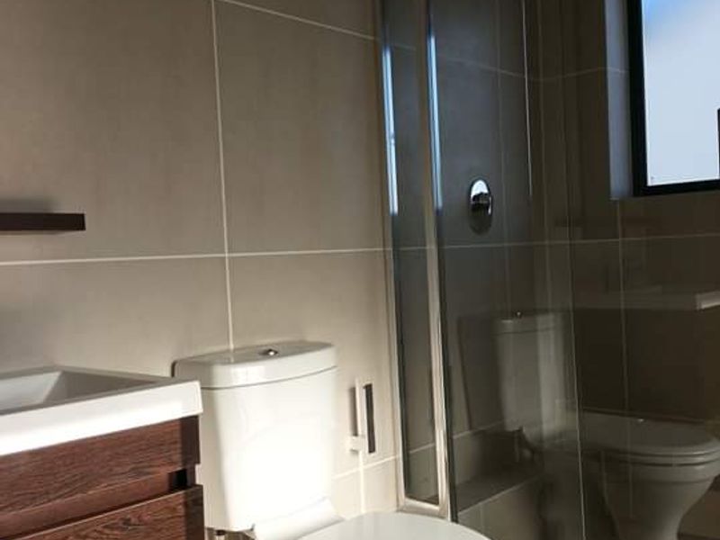 A modern bathroom featuring a glass-enclosed shower, wall-mounted vanity, and neutral tiled finishes.