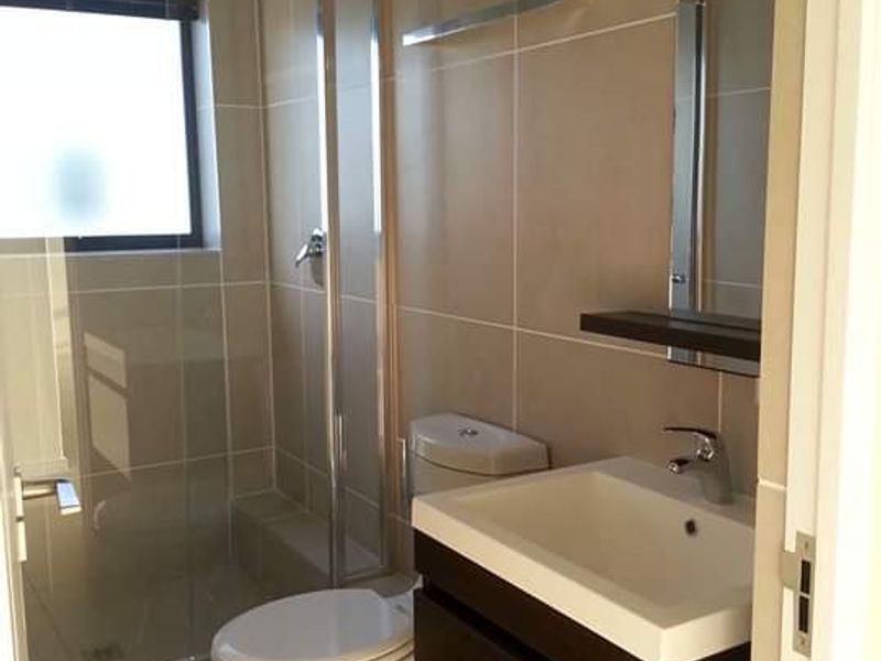 A modern, well-maintained bathroom featuring a glass shower enclosure, a wall-mounted vanity unit, and neutral floor-to-ceiling wall tiles.
