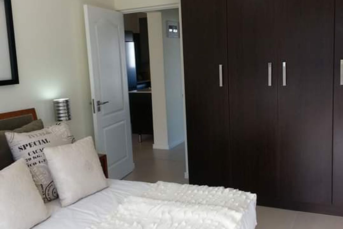 A well-maintained bedroom featuring dark wood built-in cupboards, neutral tiled flooring, and a modern pendant light fixture.