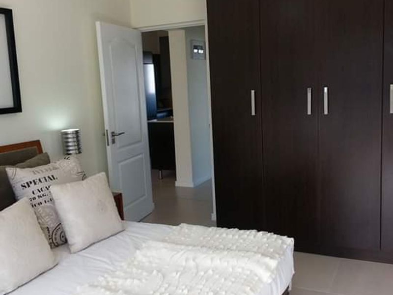 A well-maintained bedroom featuring dark wood built-in cupboards, neutral tiled flooring, and a modern pendant light fixture.
