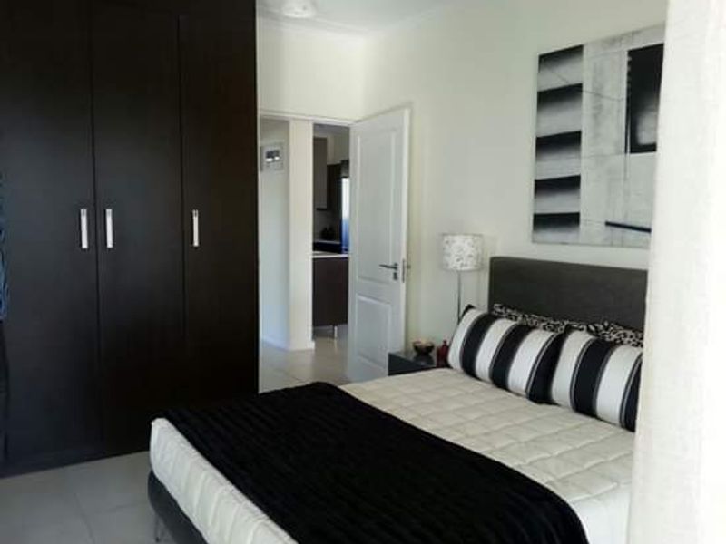A well-maintained bedroom featuring dark wood built-in cupboards, neutral tiled flooring, and direct access to the adjacent living area.