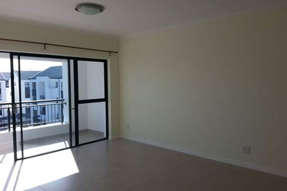 A bright, empty living room featuring neutral tiled flooring and a large sliding glass door providing access to an outdoor balcony.