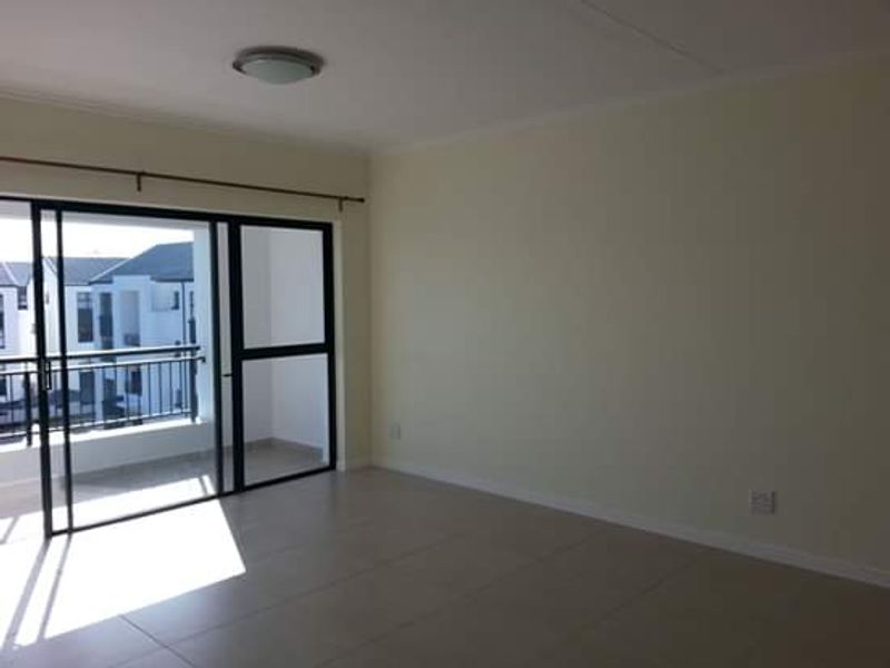 A bright, empty living room featuring neutral tiled flooring and a large sliding glass door providing access to an outdoor balcony.