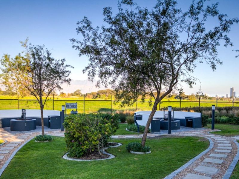 A well-maintained communal garden area featuring paved pathways, landscaped lawns, and built-in braai stations with scenic open field views.