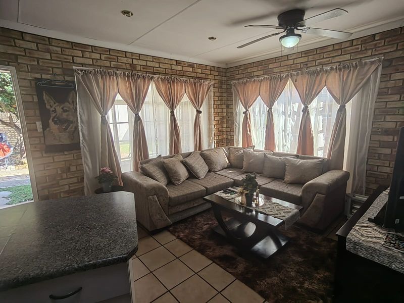 Open plan living area featuring exposed brick walls, tiled flooring, and a ceiling fan, creating a warm and textured atmosphere.