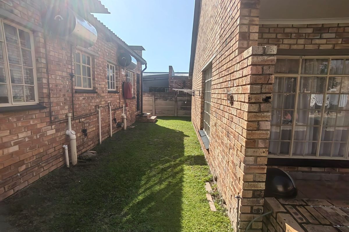 A side view of the townhouse exterior featuring exposed brick walls, solar water heating units, and a small grassed area between the building structures.