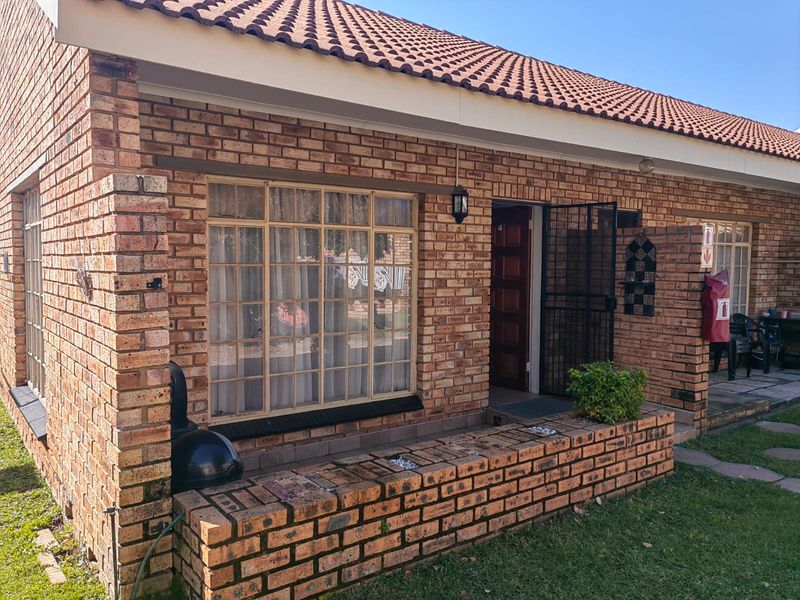Front elevation of a face brick townhouse featuring a tiled roof, secure entrance door, and a built-in brick planter box.