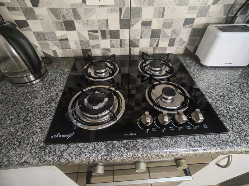 A close-up view of a modern four-burner black glass gas hob set into a granite countertop with a decorative mosaic tile backsplash.