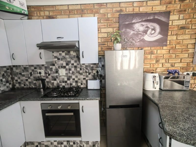 Compact kitchen featuring white cabinetry, granite countertops, a gas hob with extractor fan, and a distinctive exposed brick feature wall.