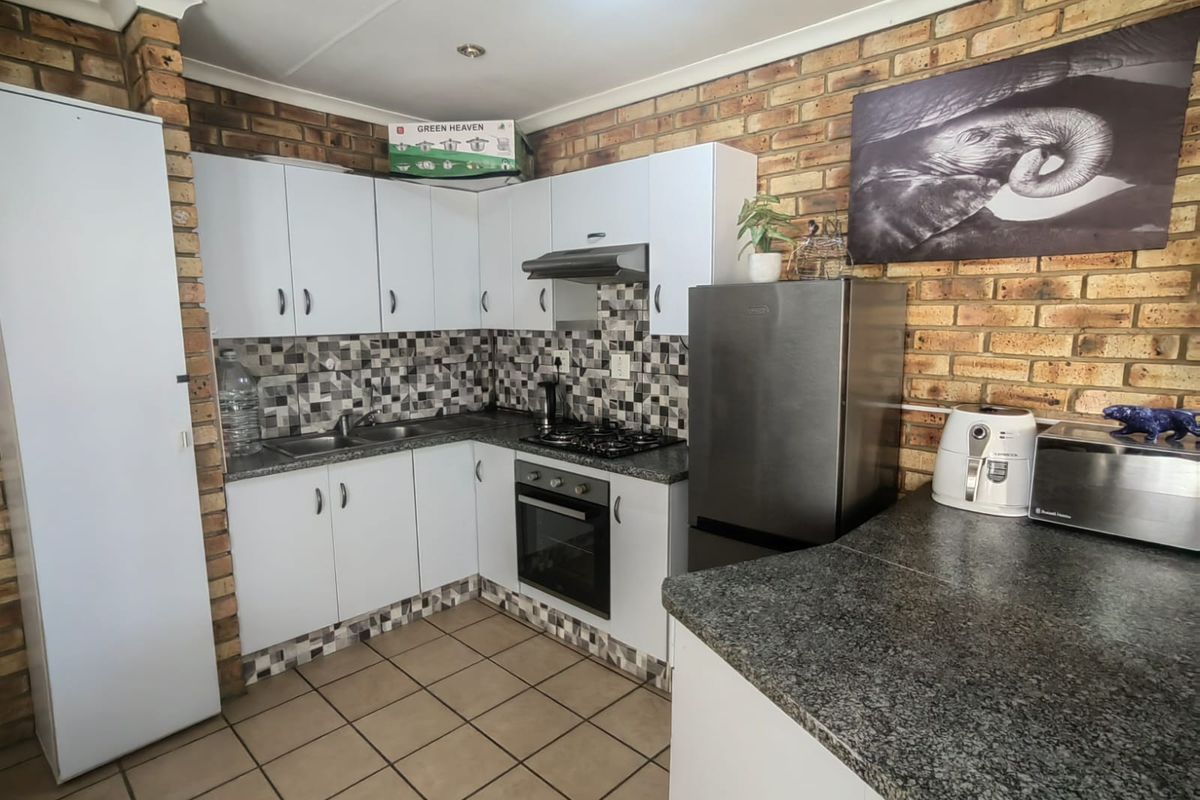 A functional kitchen featuring white cabinetry, granite countertops, a built-in oven with gas hob, and distinctive exposed brick walls with tiled flooring.